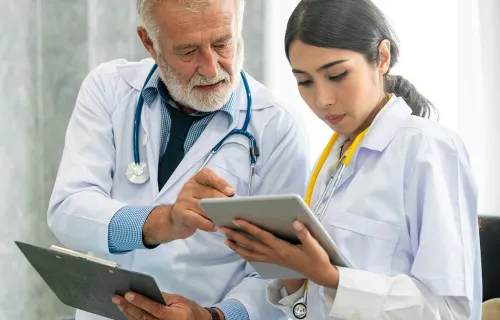 Two doctors in lab coats discuss patient reports on their tablets